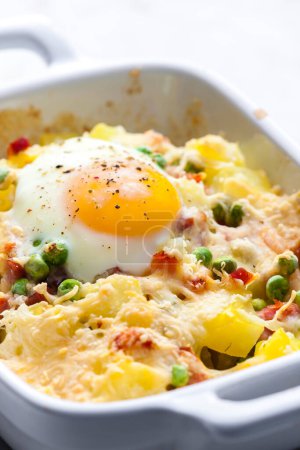 Photo for Potatoes baked with smoked meat, green peas and cheddar cheese served with fired egg - Royalty Free Image
