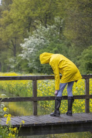 Téléchargez les photos : Young woman with yellow raincoat and rubber boots in spring nature - en image libre de droit