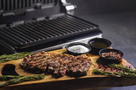 Photo for Ribeye steak on wooden board with spices and electric grill - Royalty Free Image