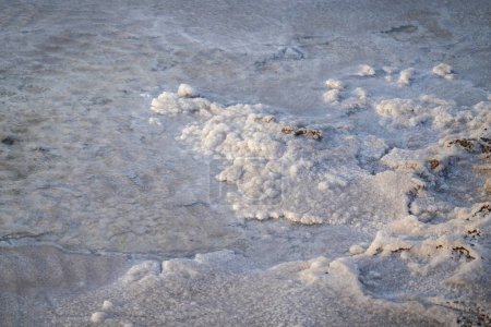 Komplizierte Strukturen und Muster von Salzablagerungen am Ufer eines ruhigen Salzsees. Das natürliche Licht unterstreicht die kristallinen Details und schafft eine ruhige und friedliche Szene.