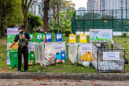 Téléchargez les photos : Bangkok, Thaïlande - 8 décembre 2022 : Un homme jette des ordures par catégories organisées par des organismes gouvernementaux à la Foire de la Croix-Rouge au parc Lumpini du 8 au 18 décembre 2022. L'image est floue à cause du mouvement - en image libre de droit