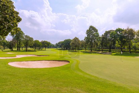 Téléchargez les photos : Vue sur un terrain de golf en Thaïlande avec de l'herbe verte luxuriante, de beaux paysages avec bunker sablonneux à côté des verts et des trous de golf. ciel bleu journée ensoleillée. - en image libre de droit