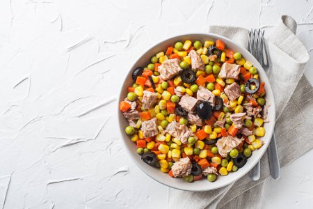 Téléchargez les photos : Salade de thon saine avec des cors, des carottes, des pois et des olives sur fond de table blanche. Salade de maïs mexicaine. - en image libre de droit