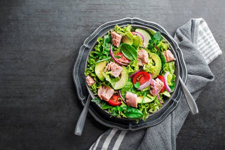 Frischer grüner Blattsalat mit Thunfisch-Avocado und Tomate auf grauem Tischhintergrund. Konzept für eine schmackhafte und gesunde Mahlzeit