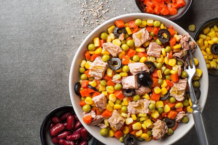 Gesunder gemischter Thunfischsalat mit Mais, Karotten, Erbsen, Bohnen und Oliven auf grauem Tischhintergrund. Mexikanischer Maissalat.
