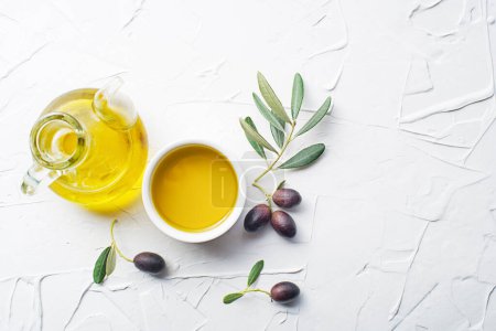 Foto de Aceite de oliva en tazón con aceitunas frescas fruta y rama de olivo sobre fondo blanco de cerca - Imagen libre de derechos
