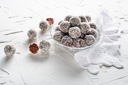 Foto de Deliciosas bolas de coco y chocolate cubiertas con coco rallado. Bolas de coco suaves, deliciosas y esponjosas con ron, galletas y chocolate - Imagen libre de derechos