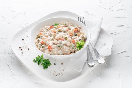 Foto de Plate of russian salad or french salad with vegetables and egg dressed with mayonnaise on white table - Imagen libre de derechos