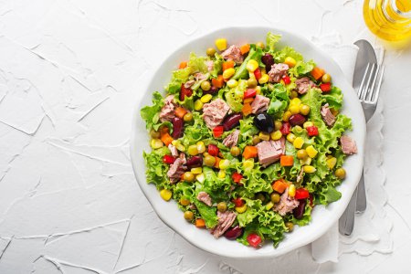 Téléchargez les photos : Healthy Green salad with tuna, corn, carrots, peas, peppers and olives on white table background. Mexican corn salad. - en image libre de droit