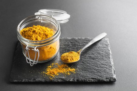 Curry powder (turmeric) in glass jar close up. Indian mixture of finely ground spices