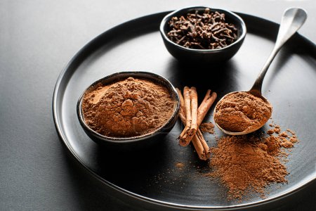 Photo for Aromatic cinnamon sticks and cup with cinnamon powder on black background close up - Royalty Free Image