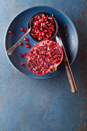 Photo for Healthy ripe pomegranate fruit opened and splitted with seeds in cup on blue background - Royalty Free Image