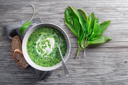 Photo for Healthy creamy soup with fresh ramson or wild garlic leaves on wooden background. Healthy spring food concept - Royalty Free Image