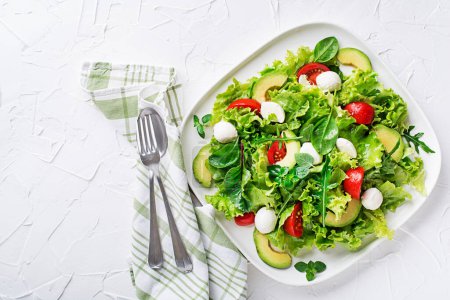 Photo for Fresh green salad with avocado, mozzarella cheese and tomato on white table background - Royalty Free Image