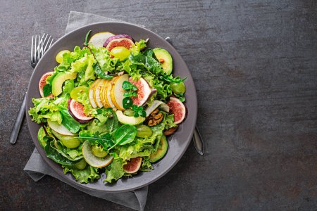 Téléchargez les photos : Salade feuillue verte fraîche avec fruits et noix sur fond de table gris. Concept pour un repas savoureux et sain - en image libre de droit