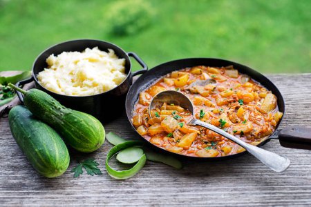Téléchargez les photos : Manger un plat traditionnel slovène avec de la sauce concombre en purée de pommes de terre rouges. Concombres fraîchement cueillis dans le jardin. Nourriture d'été - en image libre de droit