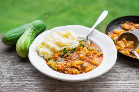 Téléchargez les photos : Manger un plat traditionnel slovène avec de la sauce concombre en purée de pommes de terre rouges. Concombres fraîchement cueillis dans le jardin. Nourriture d'été - en image libre de droit