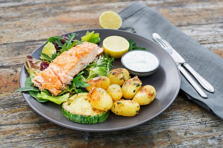 Photo for Baked salmon fillet with potatoes and vegetables on wooden table in the garden summer time - Royalty Free Image