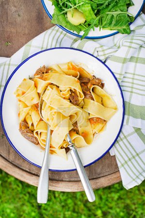 Photo for Pasta tagliatelle spaghetti with creamy sauce served on plate outside on sunny day. Eating fresh fettucine or pappardelle with meat in creamy sauce. - Royalty Free Image
