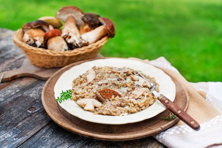 Téléchargez les photos : Délicieux risotto aux champignons habillé de parmesan et d'herbes. Panier avec des champignons porcini ingrédients en plein air le jour ensoleillé - en image libre de droit
