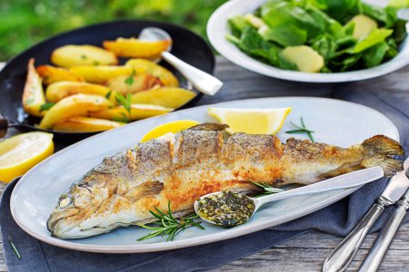 Photo for Roasted traditional river trout with salad, potatoes and (garlic, parsley) sauce, outside in the garden - Royalty Free Image