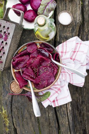 Photo for Fresh Beetroot salad with oil and herbs in bowl on wooden table in the garden - Royalty Free Image