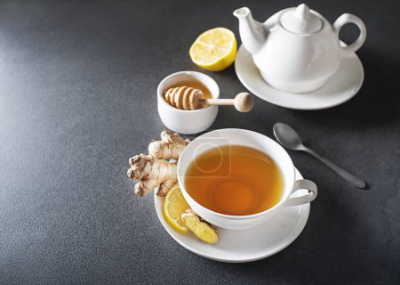 Foto de Taza de té de jengibre caliente con raíz de jengibre fresca y limón sobre fondo gris. - Imagen libre de derechos