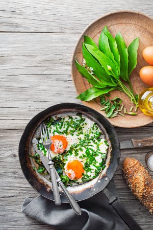 Fried eggs in a frying pan with fresh ramson or wild garlic leaves. Healthy spring diet food concept.
