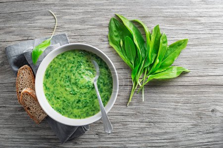 Foto de Sopa cremosa saludable con ramson fresco o hojas de ajo silvestre sobre fondo de madera. Concepto saludable de alimentos de primavera - Imagen libre de derechos