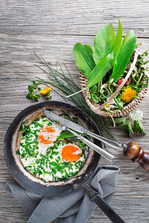 Fried eggs in a frying pan with fresh spring plants. Healthy spring diet food concept.