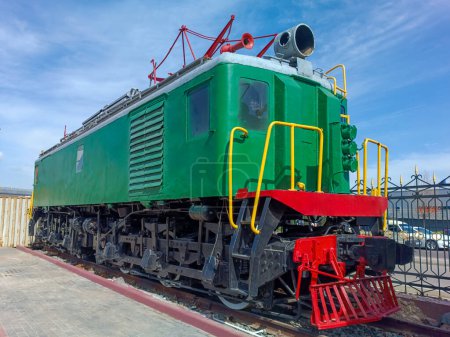 green retro electric locomotive for freight and passenger rail transportation, against the background of the sky and trees, close-up side view