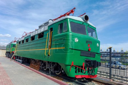 green retro electric locomotive for freight and passenger rail transportation, against the background of the sky and trees, close-up side view