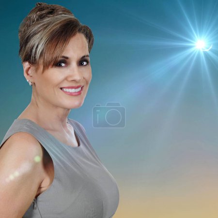 Foto de Retrato de una hermosa mujer madura con un vestido gris sobre un hermoso fondo de cielo con resplandor solar - Imagen libre de derechos
