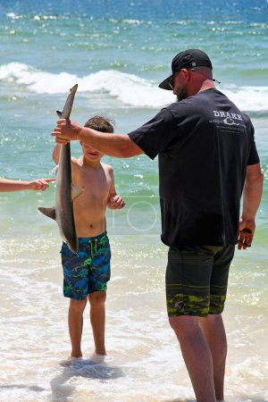 Foto de GULF SHORES, AL / USA - 3 de mayo de 2023: Joven mostrando a su hijo un shqark que pescó en Gulf Shores Beach en el Golfo de México - Imagen libre de derechos