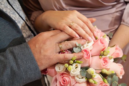 Téléchargez les photos : Anneaux de mariage sur les mains des jeunes mariés, un bouquet de fleurs en arrière-plan - en image libre de droit