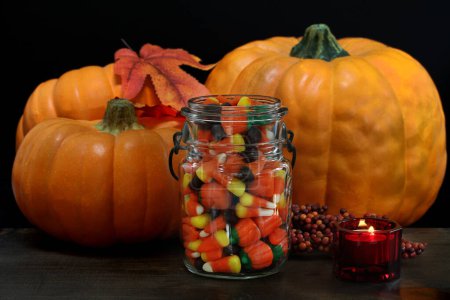 Photo for Halloween candy corn in a vintage canning jar in front of pumpkins, black background and lit candle. - Royalty Free Image