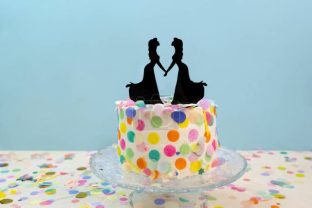 Two brides cake toppers on decorated wedding cake on blue background. Newlywed figurines decoration on wedding cake for lesbian wedding. Lesbian wedding concept LGBTQIA