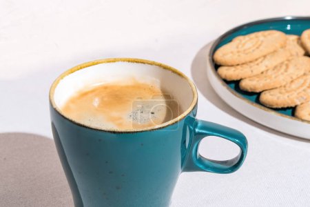 Foto de Primer plano del café en elegante taza azul con galletas recién horneadas en el plato sobre fondo blanco - Imagen libre de derechos
