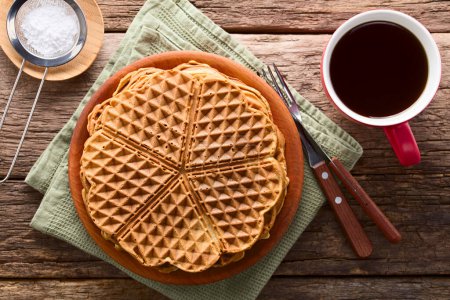 Photo for Pile of fresh homemade heart shaped waffles on wooden plate with a cup of tea and powdered sugar on the side, photographed overhead on wood (Selective Focus, Focus on the top waffle) - Royalty Free Image