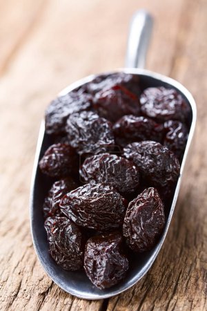 Photo for Dried plums on metal scoop on wood (Selective Focus, Focus one third into the image) - Royalty Free Image