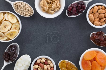 Photo for Variety of dried fruits, nuts and seeds (sunflower seed, walnut, cranberry, almond, raisin, apricot, sultana, peanut, coconut, prune, banana) in small bowls, photographed overhead on slate with copy space in the middle - Royalty Free Image