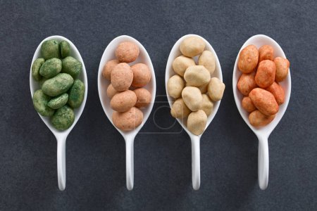 Photo for Variety of Japanese-style crunchy coated peanuts or cracker nuts with different flavoring (chives, original, chili) in small spoons, photographed overhead on slate (Selective Focus, Focus on the peanuts on the top) - Royalty Free Image