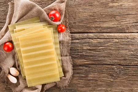 Photo for Dry uncooked ridged lasagna pasta sheets, photographed overhead on rustic wood with copy space on the side - Royalty Free Image