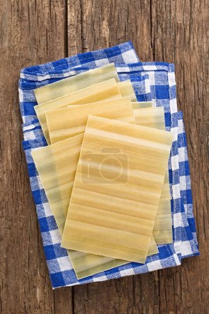 Photo for Dry uncooked ridged lasagna pasta sheets, photographed overhead on rustic wood - Royalty Free Image