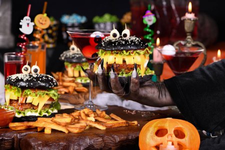 Foto de La mano de una bruja toma un cóctel de brujas con globos oculares en una copa de martini de la mesa de fiesta de Halloween. - Imagen libre de derechos