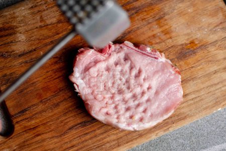 Photo for Beating meat with a hammer on a wooden board. Cooking pork chop. - Royalty Free Image