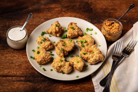 Photo for Cauliflower wings food. Pieces of cauliflower cooked in batter on a plate on a wooden background. Sprinkled with green onions. - Royalty Free Image