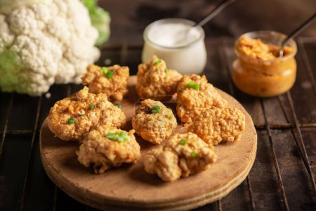 Photo for Pieces of flour-fried cauliflower with vegan sauces on a plate on a dark background. Cauliflower wings food. - Royalty Free Image