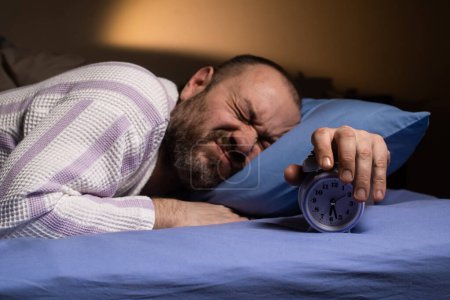 Photo for Annoying alarm clock in the morning. Dislike waking up in the morning. The man is aggressively awakened by the ringing of the alarm clock. Hateful morning. - Royalty Free Image