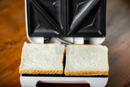Two fresh toasts lie in open sandwich maker. Preparation for preparation of toasts.